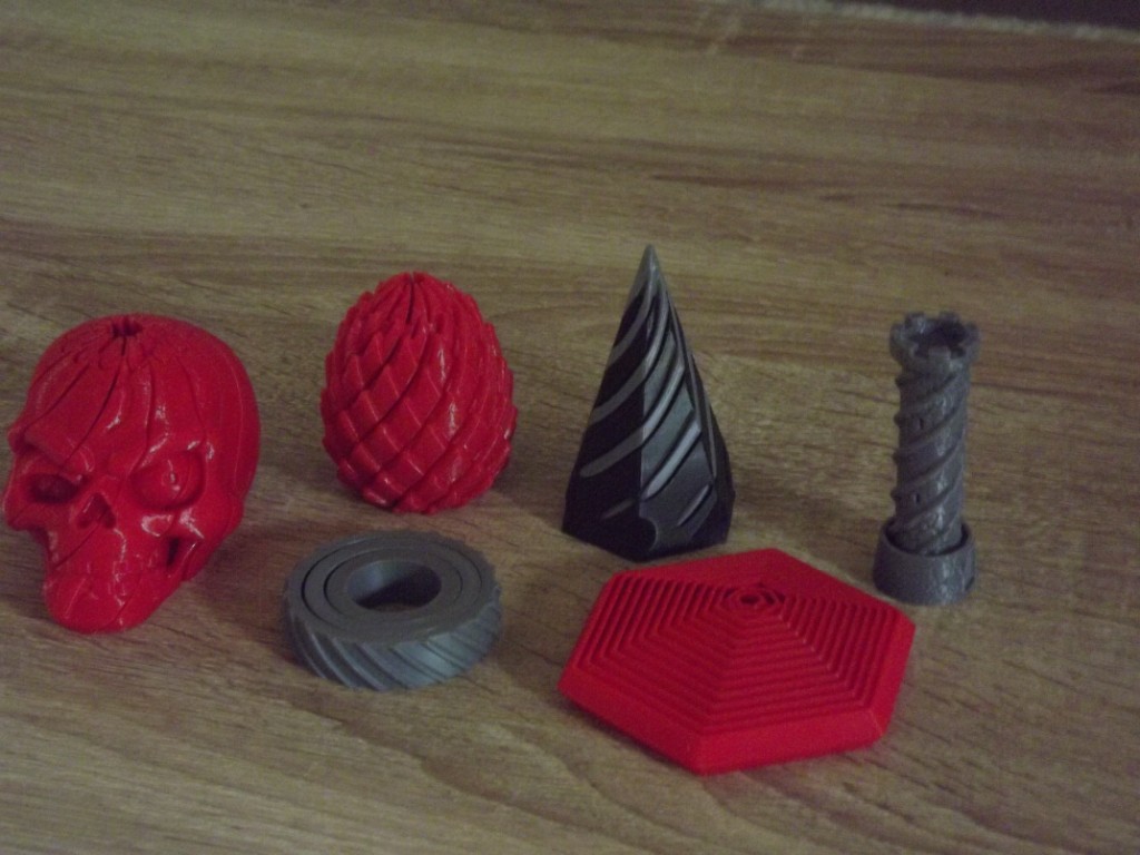 3D-printed fidgets in red and gray: skull, dragon egg, ring, spiral, hexagon, and tower